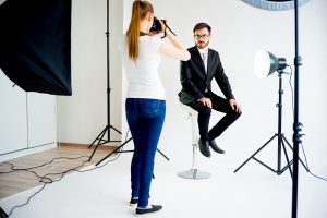 Female photographer taking picture of a male model in studio